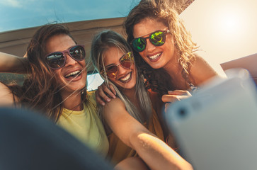 Three female friends enjoying traveling in the car. Sitting in rear seat and and making selfie.	