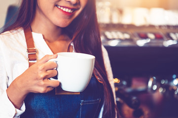 Closeup of professional female barista hand making and holding white cup of coffee. Happy young woman at counter bar in restaurant background. People lifestyles and Business occupation concept