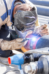 Construction worker welding pipes on a heavy site.