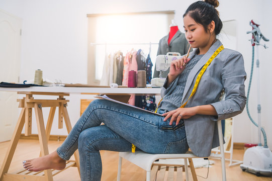 Attractive Asian Female Fashion Designer Working In Home Office Workshop. Stylish Fashionista Woman Creating New Cloth Design Collection. Tailor And Sewing. People Lifestyle And Occupation Concept