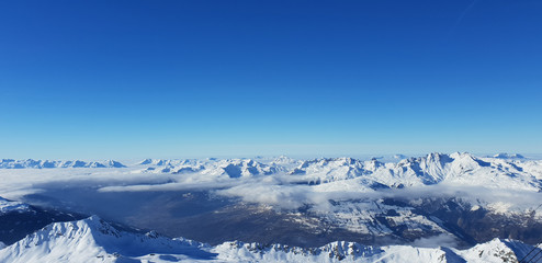 Fototapeta na wymiar Panoramic view above clouds in valley of snowy mountain in european Alps