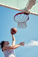 Image of sports man throwing ball into basketball hoop on sports field on street on summer day .
