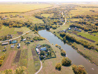 Drone aerial view of the village at summer season. Roofs of the houses and farms between grass fields and trees. Birds-eye view of  pond in settlement. Penza region, Russia.Idyllic rural landscape.