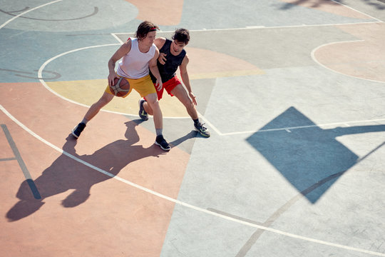 Top view photo of two athletes men playing basketball on playground in morning.