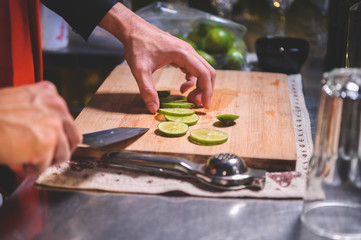 Closeup of professional bartender hand slicing lemon for making lemonade juice by knife in night club. Chef making drinks for guest in pub restaurant. Food and beverage concept.
