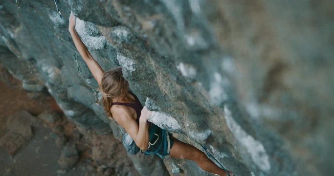 Cinematic slow motion rock climbing moment - strong fit woman makes a big reaching move on over hanging rock wall