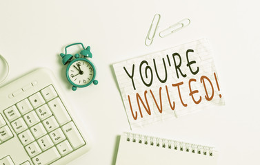 Writing note showing You Re Invited. Business concept for make a polite friendly request to someone go somewhere Blank paper with copy space on the table with clock and pc keyboard