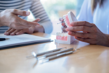 Dentist showing and explaining teeth disease treatment to patient using teeth model denture and explorer mirror tool in dental clinic office. Healthcare concept.