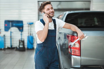 young handsome mechanic wearing uniform leaning on pickup trunk talking on the phone in car service center © studioprodakshn