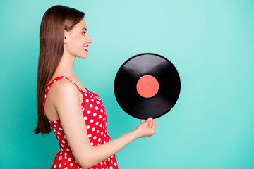 Profile side photo of lovely girl holding gramophone disc wearing polka dot dress skirt isolated over teal turquoise background