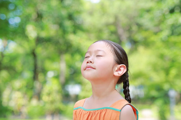 Portrait of happy Asian child close their eyes in garden with Breathe fresh air from nature. Close up kid girl relax in green park for good health.