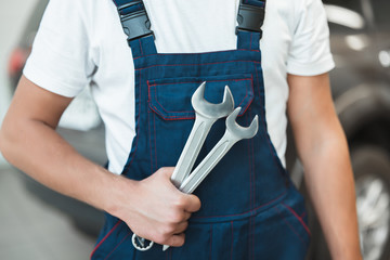 mechanic wearing uniform holding two spanners in car service center