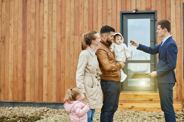 Caucasian family of four stand outdoor near new house just sold.
