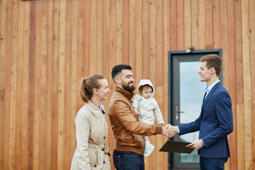 Caucasian happy family and realtor wear blue suit stand outdoor near new house just sold. Men shake...