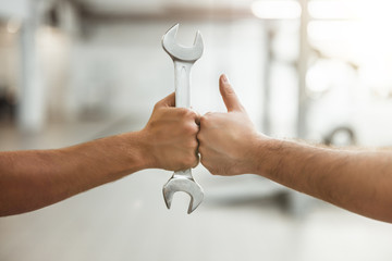 two man fist bumping one holding car spanner another showing like sign
