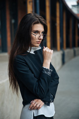 Young beautiful brunette girl, office clothing style, sitting on the street at a table in a cafe, street model posing style, makes notes in a notebook, talking on the phone