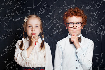 Smart little children thinking. Little boy and girl student on blackboard background with science and maths formulas