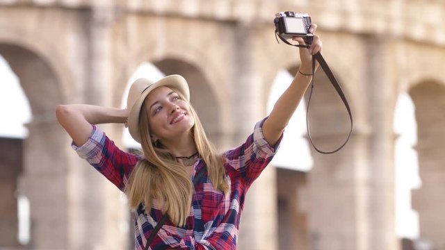 Young blonde woman with blue eyes and long hair, taking selfie with a vintage camera at Colosseum, Rome.