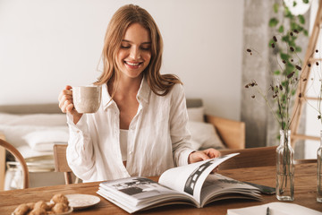 Woman sit indoors in office reading magazine drinking coffee.