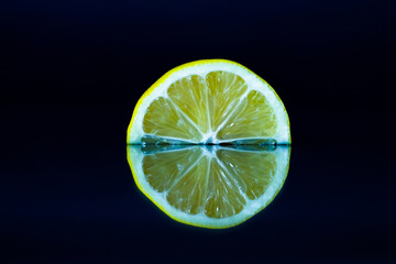 Lemon slice on black reflective background. Creative food concept, minimal style.