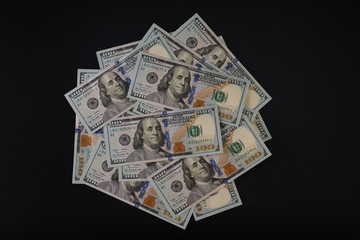 A pile of one hundred dollar bills on a black background