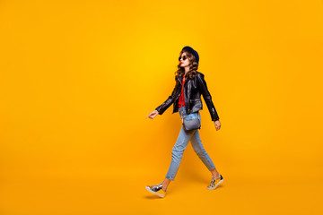 Full length profile side photo of focused gorgeous girl walk on stroll wear black leather jacket denim jeans isolated over yellow color background
