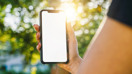 Mockup image of woman's hands holding black smartphone with white blank screen on a in the park