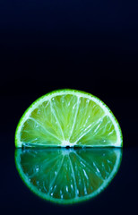 Lime slice on black reflective background. Creative food concept, minimal style.