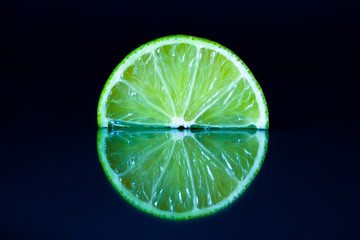 Lime slice on black reflective background. Creative food concept, minimal style.