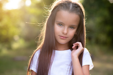 Pretty little girl with long brown hair posing summer nature outdoor. Kid's portrait. Beautiful child's face
