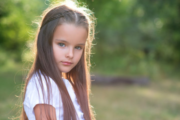 Pretty little girl with long brown hair posing summer nature outdoor. Kid's portrait. Beautiful child's face