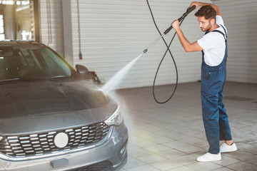 young handsome man washing car at car washing station using high pressure water