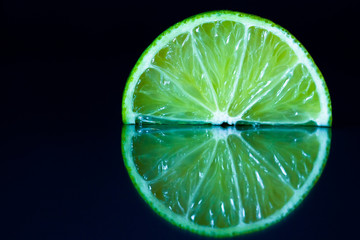 Lime slice on black reflective background. Creative food concept, minimal style.