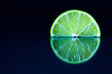 Lime slice on black reflective background. Creative food concept, minimal style.