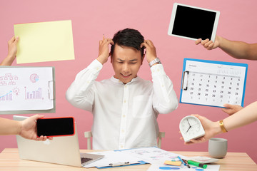 Sad young man sits at desktop, hands with papers, alarm clock, touchpad, notepad with stickers,...