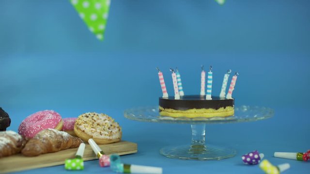Party&rsquo;s over. Dolly tracking shot of a birthday party. Birthday cake with blow out candles, sweets donuts, muffins, croissant, party horns and a green banner on the blue background. Happy anniversary.