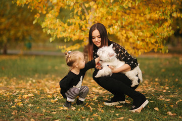 Mother and little daughter walking with her dog in autumn weather. Stylish little daughter and her beautiful mother. Happy childhood. Outdoors portrait of happy family.