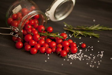 red small cherry tomatoes summer and autumn harvest in a glass jar with salt pepper rosemary on a black background scattered
