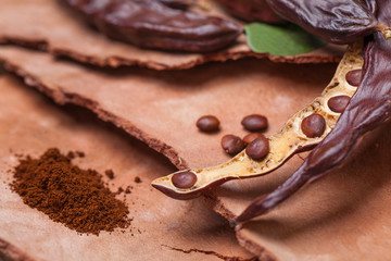 Carob. Organic carob pods with seeds and leaves on tree bark table. Healthy eating, food background.