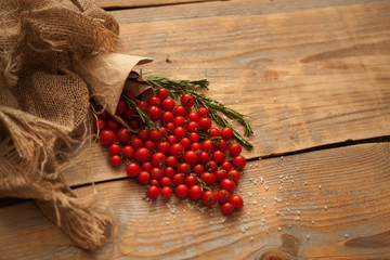 small red cherry tomatoes on a clay plate in burlap scattered on a wooden table rosemary leaves coarse salt and black pepper