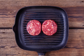 Top view of two raw beef burger meats on grill pan on a wooden background.