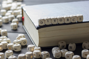 Word - Divorce made up of wooden letters on the table with wedding rings.
