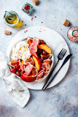 Summer fruit salad with burrata, peaches, figs, grapes and jamon or prosciutto. Top view, overhead