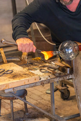 Glass blowing artist making crystal vase in high temperature flame