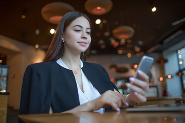 Confident woman successful entrepreneur reading e-mail on cell telephone while sitting in modern restaurant interior during recreation time. Female skilled manager using messenger on smartphone