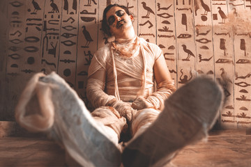 A man sits leaning on a wall wearing of helloween costume