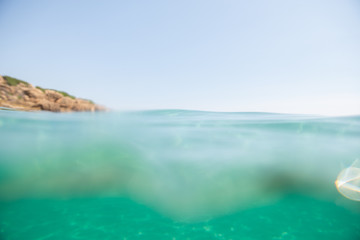 Turquoise blue sea above water surface and underwater. Sun glare at the bottom of ocean. Waves underwater and rays of sunlight shining through. Transparent water and light at sand.