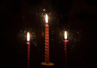 Three blurred red candles burning in the darkness outside the window