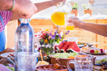 Group of hands sharing food and drink. Caucasian peoples enjoying brunch or meal together. Fruits and vegetables on the wooden table. Sunlight outdoor on the terrace