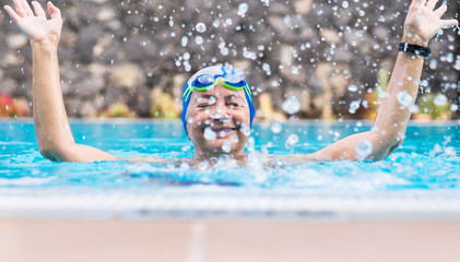 Cheerful senior people in activity in the swimming pool. Healthy lifestyle. Partially hidden by the water drops. With cap and googles. People smiling and playing sports